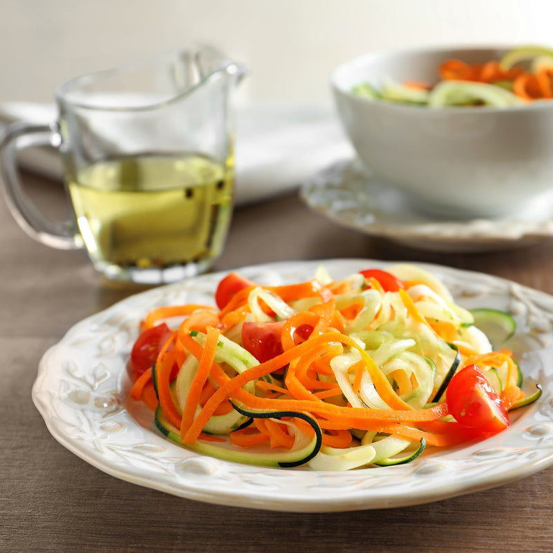 Lifestyle image of a plate of shredded raw vegetables with a glass jar of salad oil