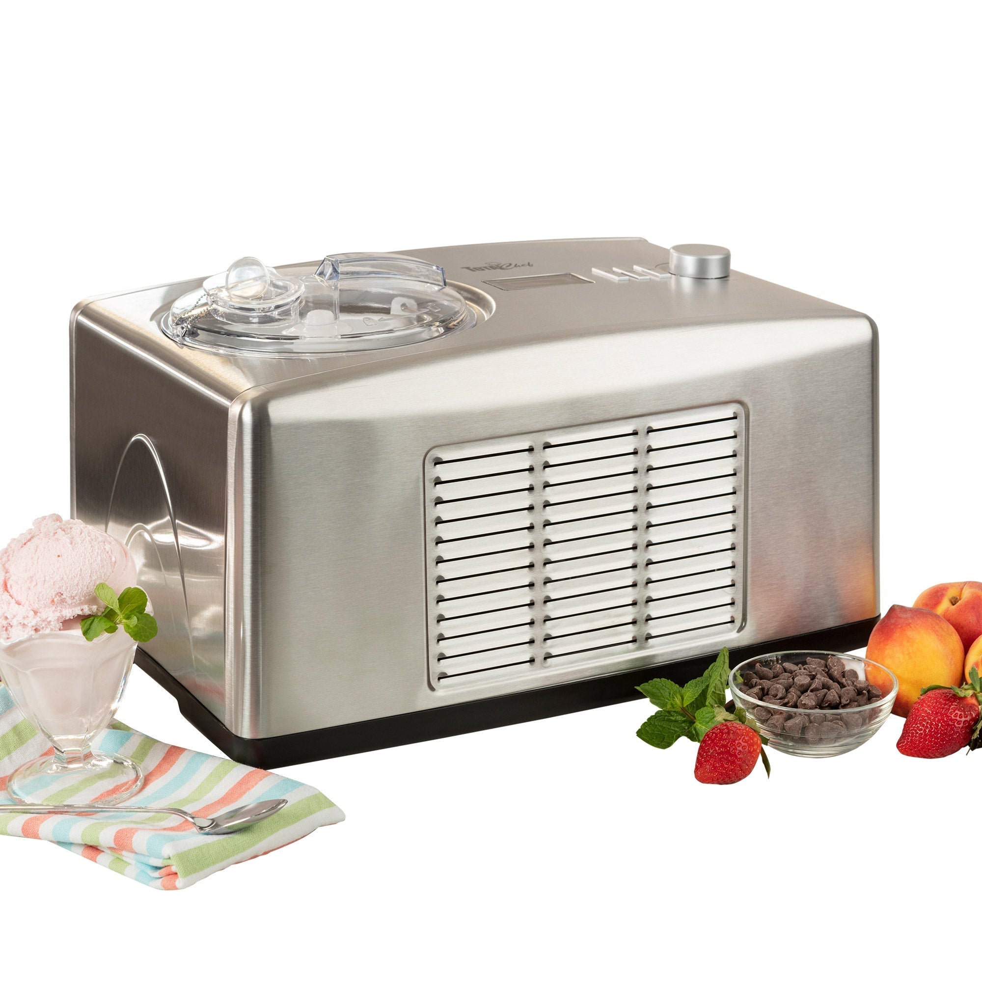 Product shot of ice cream maker on white background with a cup of light pink ice cream and a striped napkin to the left and fruits and chocolate chips on the right