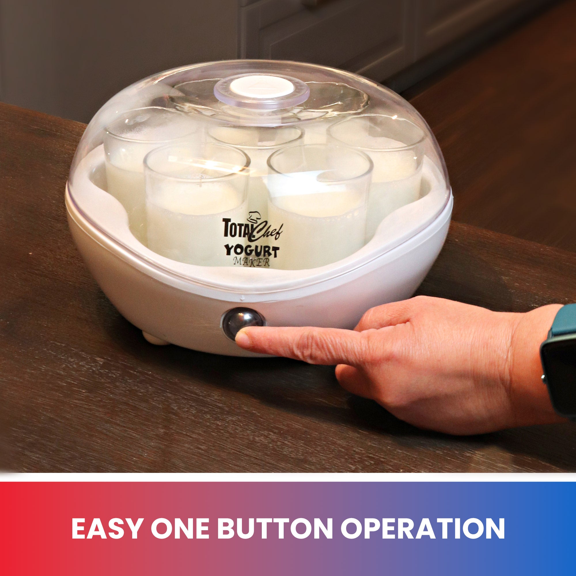 Lifestyle image of the closed yogurt maker with jars of milk mixture inside on a dark brown tabletop, and a person's finger pushing the power button. Text below reads, "Easy one button operation"