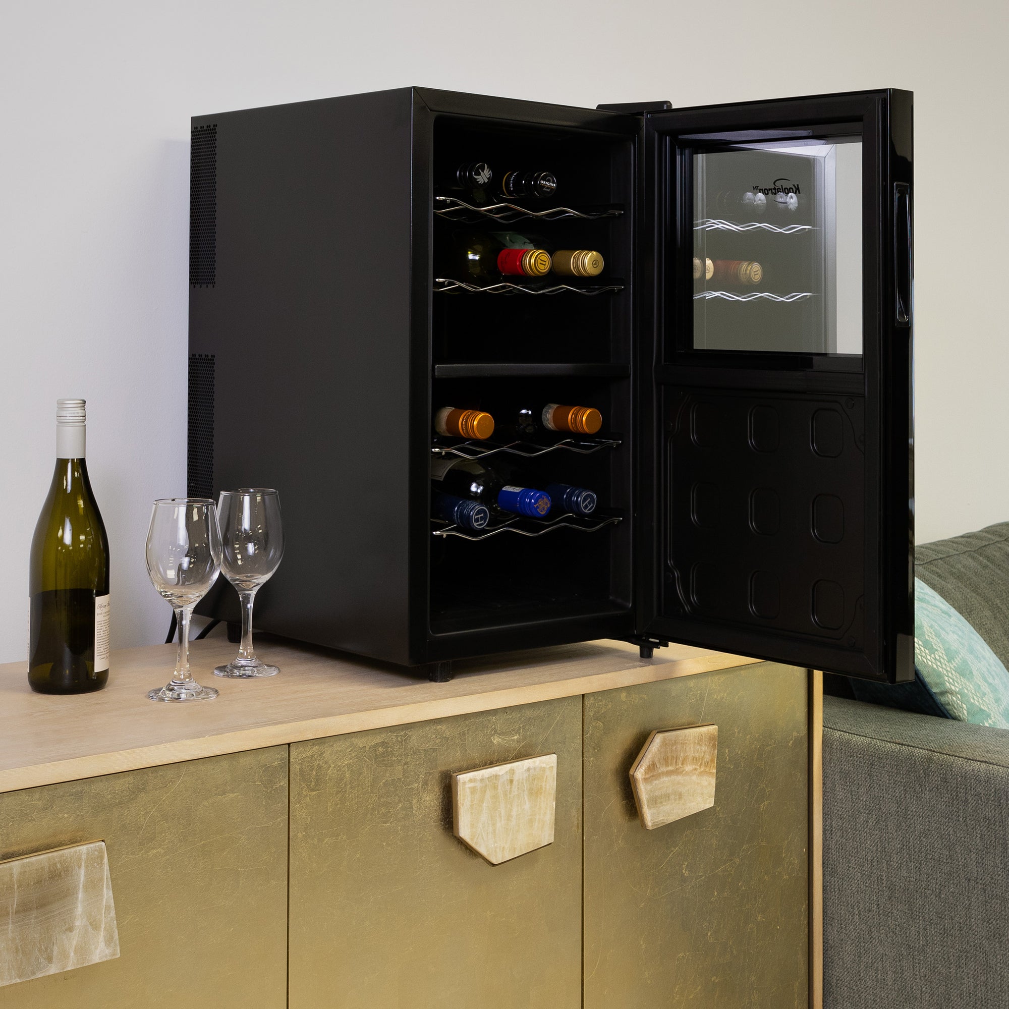 Koolatron 18 bottle dual zone wine cooler, open and filled with bottles of wine, on a gold-coloured sideboard with a bottle of wine and one glass beside it