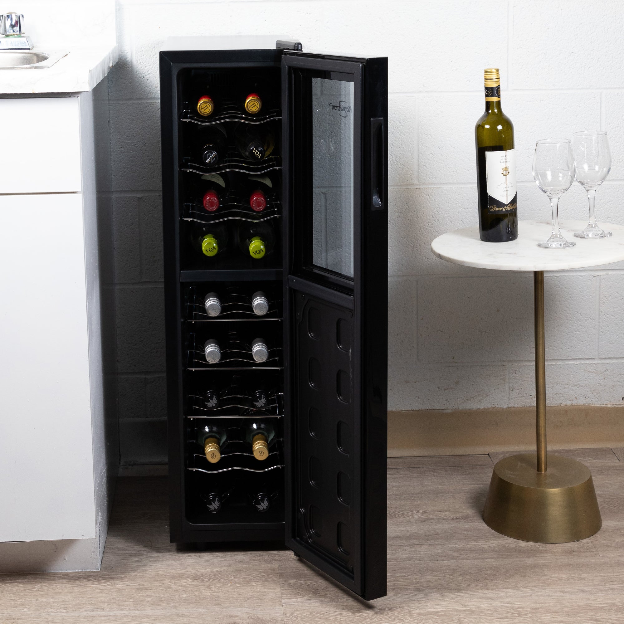 Koolatron 18 bottle dual zone wine cooler, open and filled with bottles of wine, on a gold-coloured sideboard with a bottle of wine and one glass beside it