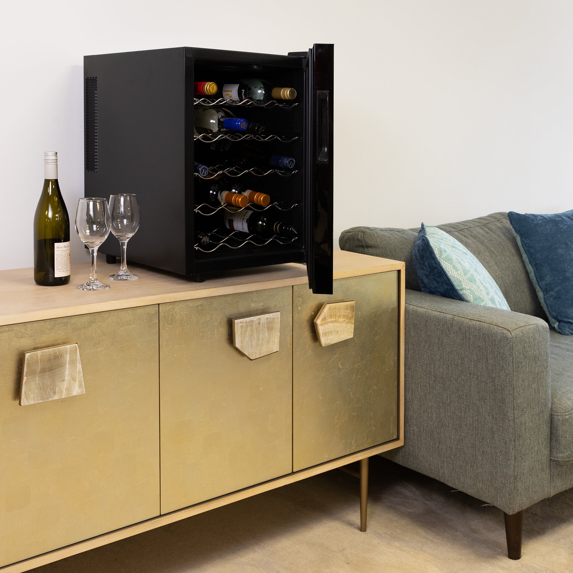 Koolatron 20 bottle wine cooler, open and filled with bottles of wine, on a gold-coloured sideboard with a bottle of wine and one glass beside it