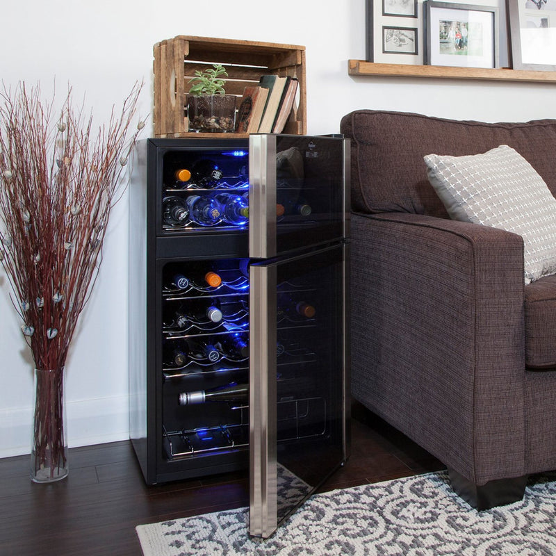 Lifestyle image of wine fridge, open and filled with bottles of wine, on a reddish-brown hardwood floor with a white and blue area rug in front, a brown sofa to the right, and a glass vase full of red sticks on the left